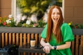 Portrait of pleased redhead young woman winking, sitting at table with coffee cup and mobile phone in outdoor cafe Royalty Free Stock Photo