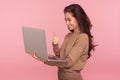 Portrait of pleased young woman in casual sweater holding laptop and showing thumbs up while talking on video call