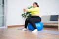 Portrait plus size woman doing exercise with fitness ball in home gym. Overweight woman sitting on a pilates ball and Stretching Royalty Free Stock Photo