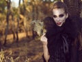 Portrait of posh dangerous lady vampire in the woods holding delicate mask and looking straight with predatory gaze. Royalty Free Stock Photo