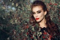 Portrait of posh redheaded woman with provocative make up standing in the berry bush and looking straight with predatory gaze