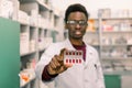 Portrait of positive African American man pharmacist in modern drugstore holding red pills in the hand. Focus on the Royalty Free Stock Photo