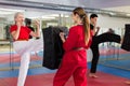 Aged woman kicking shield in martial arts training at gym