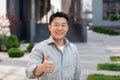 Portrait of positive asian man standing outdoors and gesturing thumb up, walking in urban city area, copy space Royalty Free Stock Photo
