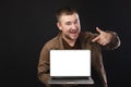 Portrait of a positive bearded man in casual clothes holding a laptop and pointing at a blank screen, excited, happy Royalty Free Stock Photo