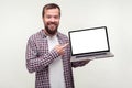 Portrait of positive bearded man in casual plaid shirt holding laptop and pointing at empty screen. white background, place for ad Royalty Free Stock Photo