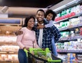 Portrait of positive black family with shopping cart smiling and looking at camera at modern supermarket Royalty Free Stock Photo
