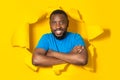 Portrait of positive black man posing with folded arms in torn paper hole, looking and smiling at camera Royalty Free Stock Photo