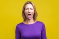 Portrait of positive carefree woman demonstrating tongue. indoor studio shot isolated on yellow background