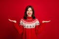 Portrait of positive cheerful cute woman with bob hairdo dressed red sweater hold palms compare products isolated on red
