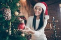 Portrait of positive cheerful girl in santa claus headwear hang christmas ball on evergreen tree for x-mas newyear Royalty Free Stock Photo