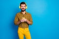 Portrait of positive cheerful man enjoy leisure time listen music melody use smartphone wear headset bright plaid pants