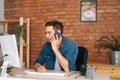 Portrait of positive confident young freelancer male talking on mobile phone sitting at desk with desktop computer at Royalty Free Stock Photo