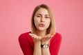 Portrait of positive female wears red sweater and trendy watch, blows kiss as flirts with someone, expresses love and good feeling Royalty Free Stock Photo