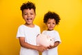 Portrait of positive funky small kids arms hold money savings pig bank isolated on yellow color background