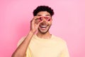 Portrait of positive funny pleasant man with afro hairstyle earrings stubble looking in binoculars isolated on pink