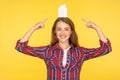 Portrait of positive ginger girl in casual shirt pointing paper house on her head and smiling at camera, dreaming of own