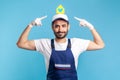 Portrait of positive handyman, mover guy in workwear and safety gloves pointing paper house Royalty Free Stock Photo