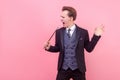 Portrait of positive illusionist with magic wand pretending to sing with stick. isolated on pink background, copy space