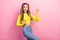 Portrait of positive impressed girl ponytails dressed yellow long sleeve clenching fists scream yeah isolated on yellow