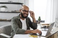 Portrait of positive latino male freelancer working on laptop and smiling at camera, sitting at desk at home, free space Royalty Free Stock Photo