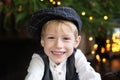 Portrait of positive little boy in cap against backdrop of Christmas tree with garland lights. Sincere child emotions. Happy child Royalty Free Stock Photo