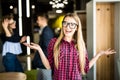 Portrait of a positive looking young woman standing with her open palms with coworkers talking in the background. Royalty Free Stock Photo