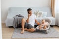 Portrait of positive optimistic man wearing white casual style T-shirt and jeans short sitting on floor and talking phone, Royalty Free Stock Photo