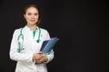 Portrait of Positive Professional Female GP Doctor Posing in Doctor`s Smock and Endoscope Against Black