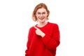 Portrait positive redhead young woman in red christmas sweater smiling pointing finger at empty copy space for text or product Royalty Free Stock Photo