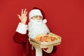 Portrait of positive Santa Claus in glasses isolated with pizza box in hands on red background, looking into camera. Man in red Royalty Free Stock Photo