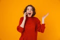 Portrait of positive woman holding and speaking on cell phone while standing isolated over yellow background Royalty Free Stock Photo