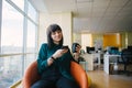 Portrait of positive young business woman sitting in modern office smiling and looking at the phone.