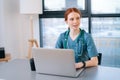 Portrait of positive young female doctor in blue green medical uniform typing on laptop keyboard sitting at desk on Royalty Free Stock Photo