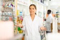 Portrait of a positive young female pharmacist in a pharmacy, standing in the trading floor Royalty Free Stock Photo