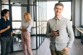 Portrait of positive young male office worker in casual clothes holding takeaway coffee cup in hand standing in office Royalty Free Stock Photo