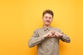 Portrait of positive young man in shirt and glasses on yellow background, shows with hands gesture of heart with closed eyes and Royalty Free Stock Photo