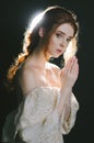 Portrait of a praying young red-haired woman in vintage ash dress with open shoulders on a black background in backlight. A prince Royalty Free Stock Photo