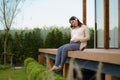 Portrait of pregnant Happy Asian woman sitting on terrace at home and using smart phone for listening music in headphones Royalty Free Stock Photo