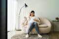 Portrait of pregnant Happy Asian woman sitting on sofa at home and using smart phone for listening music in headphones Royalty Free Stock Photo