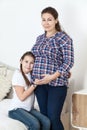 Portrait of pregnant mother with young daughter listening the belly, people are together in bedroom