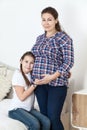 Portrait of pregnant mother with young daughter listening the belly, people together in bedroom