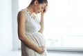 A portrait of pregnant woman has headache staying near window at home