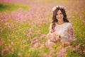 Portrait of a pregnant woman with teddy bear in fieid of pink flowers. Young beautiful pregnant girl with a wreath on her head in Royalty Free Stock Photo