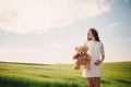 Portrait of a pregnant woman with teddy bear in hand in the field of grass. Young beautiful pregnant girl with a wreath on her Royalty Free Stock Photo