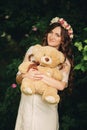 Portrait of a pregnant woman with teddy bear in hand outdoors. Young beautiful pregnant girl with a wreath on her head Royalty Free Stock Photo
