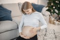 Pregnant lady sitting near a sofa in living room and touching her belly Royalty Free Stock Photo