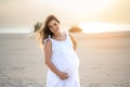 Portrait of pregnant woman wearing white dress posing on the beach at sunset. Royalty Free Stock Photo