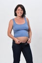 Portrait of a pregnant woman woman buttoning her jeans on white background