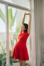 Portrait of pregnant young woman stretching joyfully standing in livingroom lit by warm sunlight, copy space